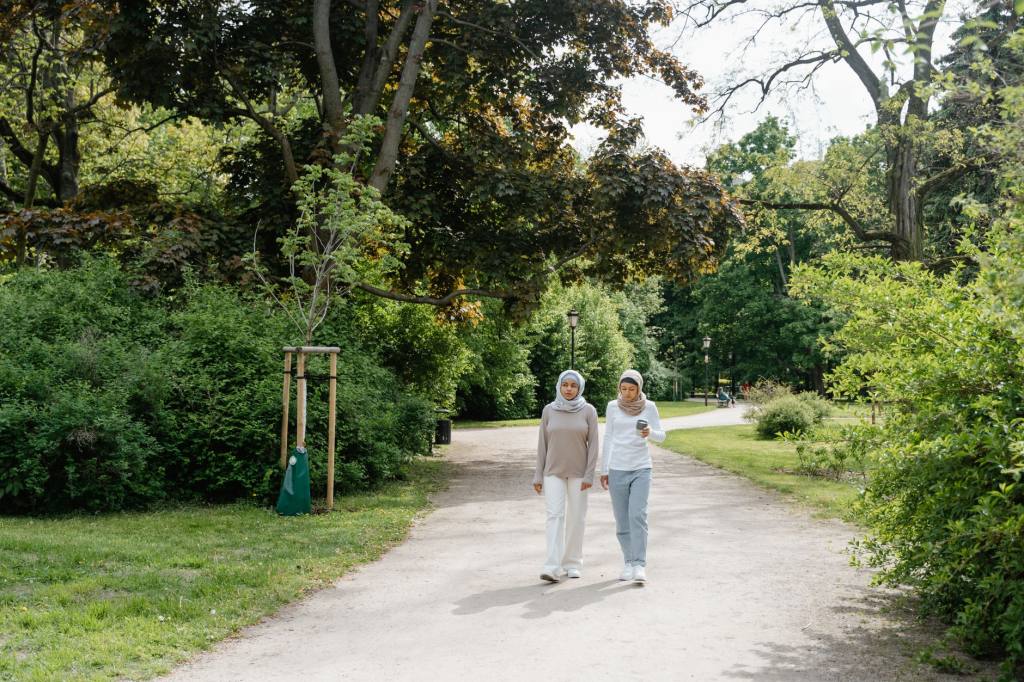 Two women wearing hijabs enjoy a peaceful walk in a lush green park.