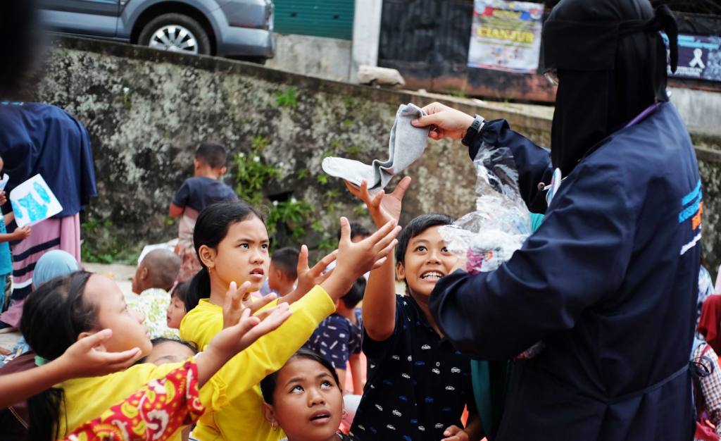 Volunteers give clothes to eager children in a lively outdoor setting.
