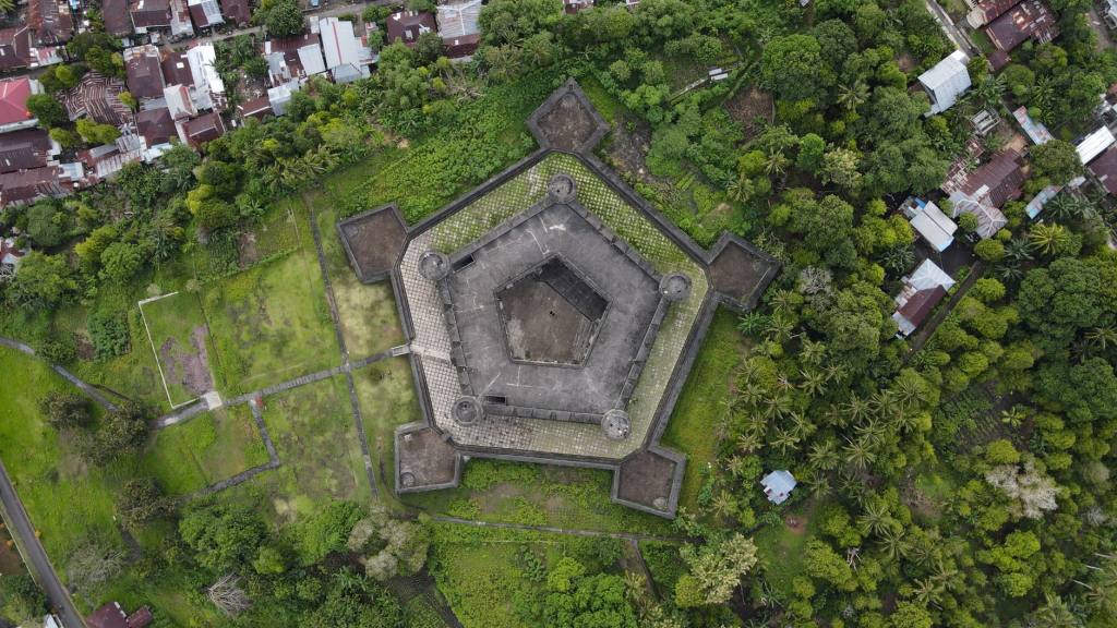 A top-down view of a historic fortified structure surrounded by greenery and adjacent buildings.