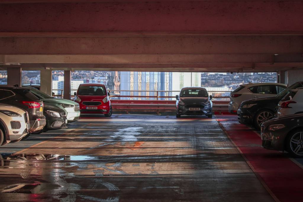 Parked cars in a multi-level parking garage overlooking a cityscape.